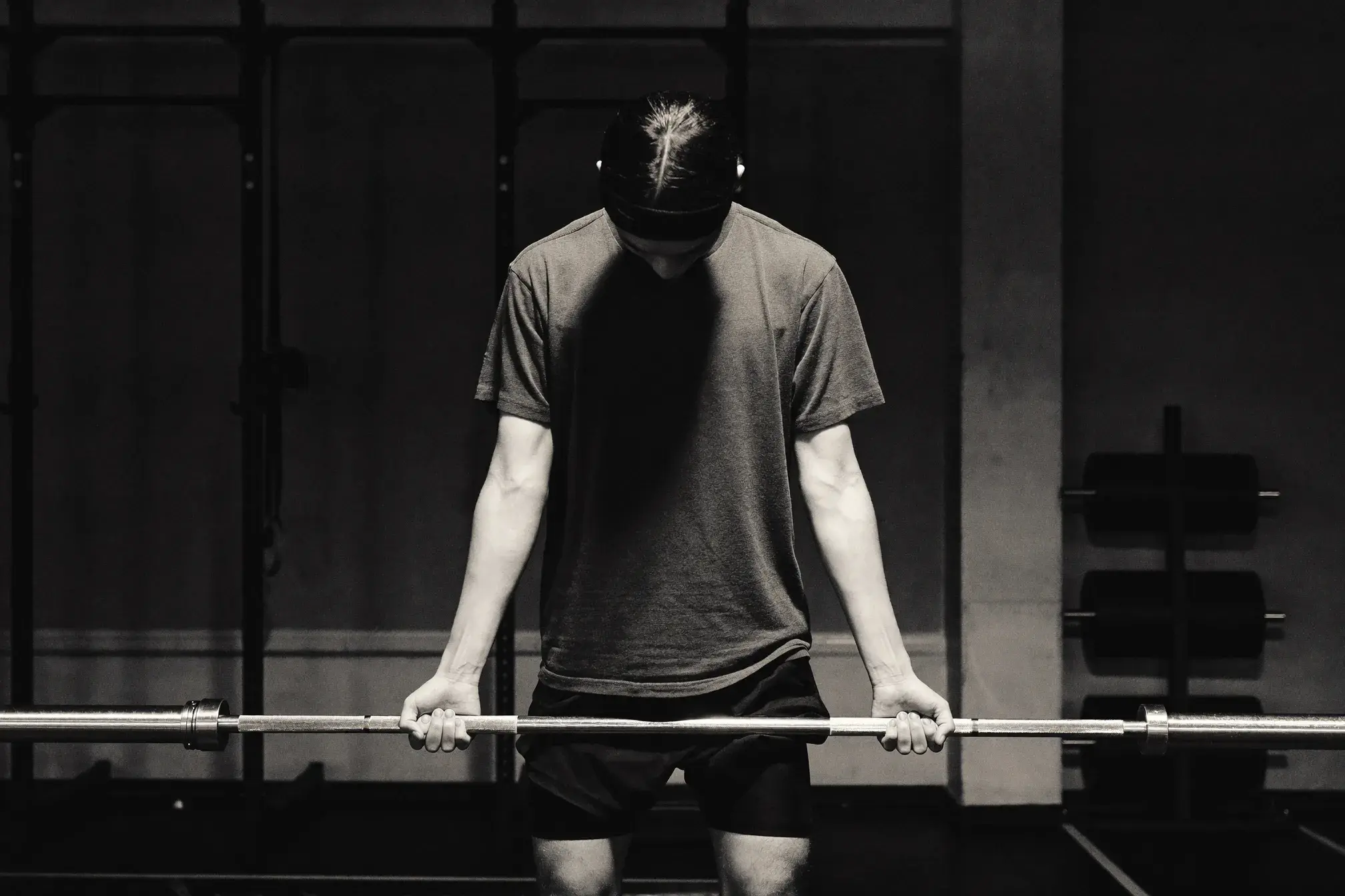 First-time lifter gripping an empty barbell with hands bowed in prayer posture — how to start lifting weights as a Christian