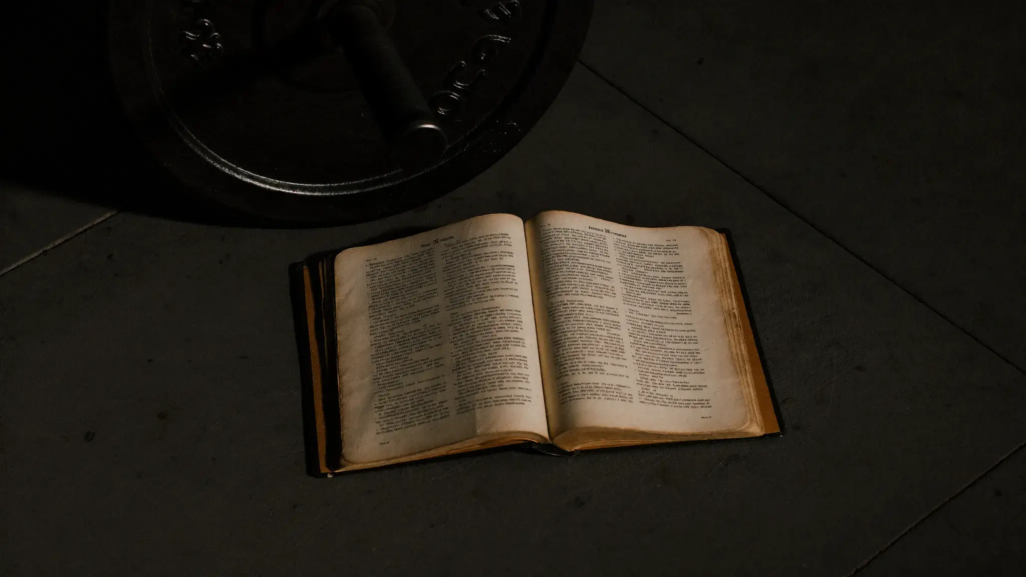 Open Bible next to a barbell plate on a gym floor — faith and strength training as stewardship