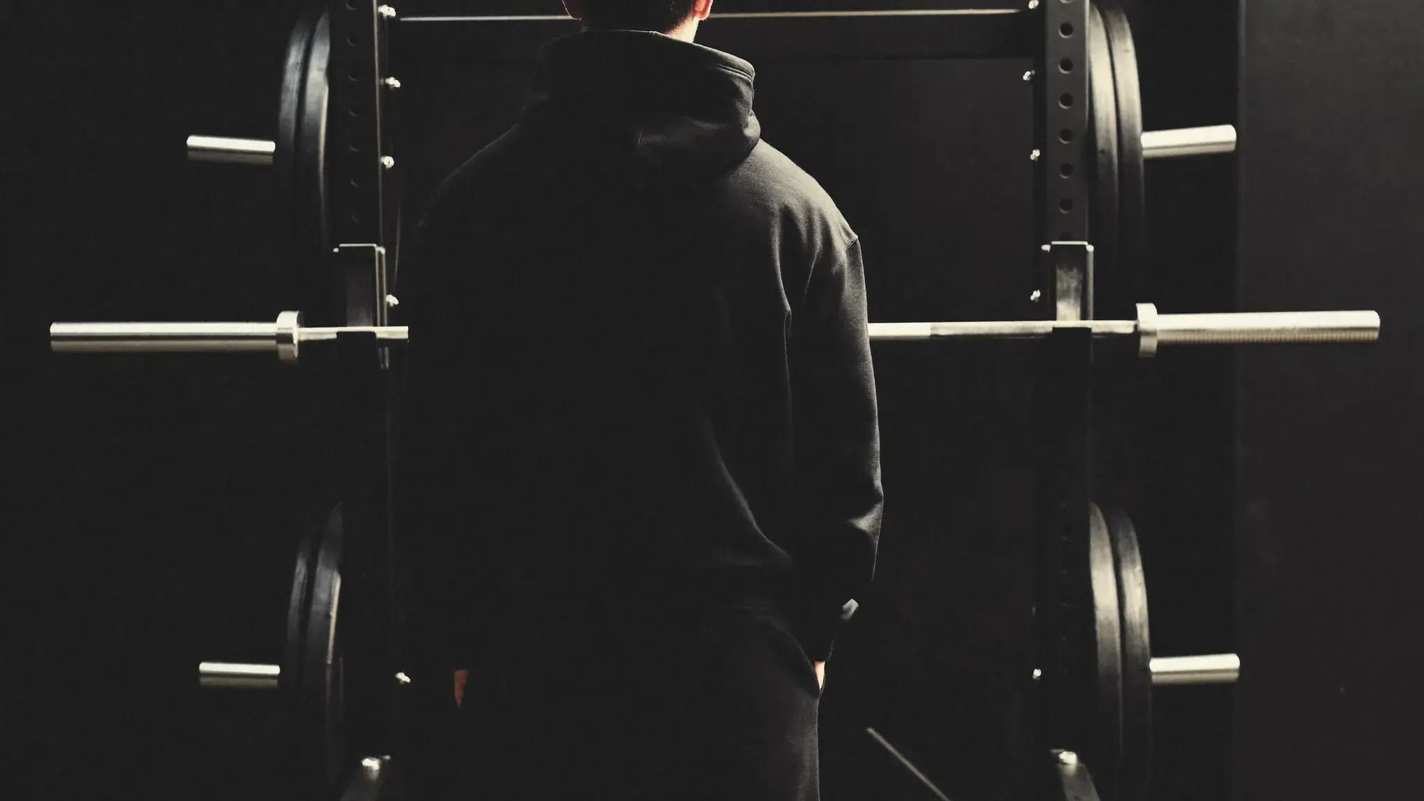 Athlete standing quietly at a barbell rack in a gym — faith-driven training identity