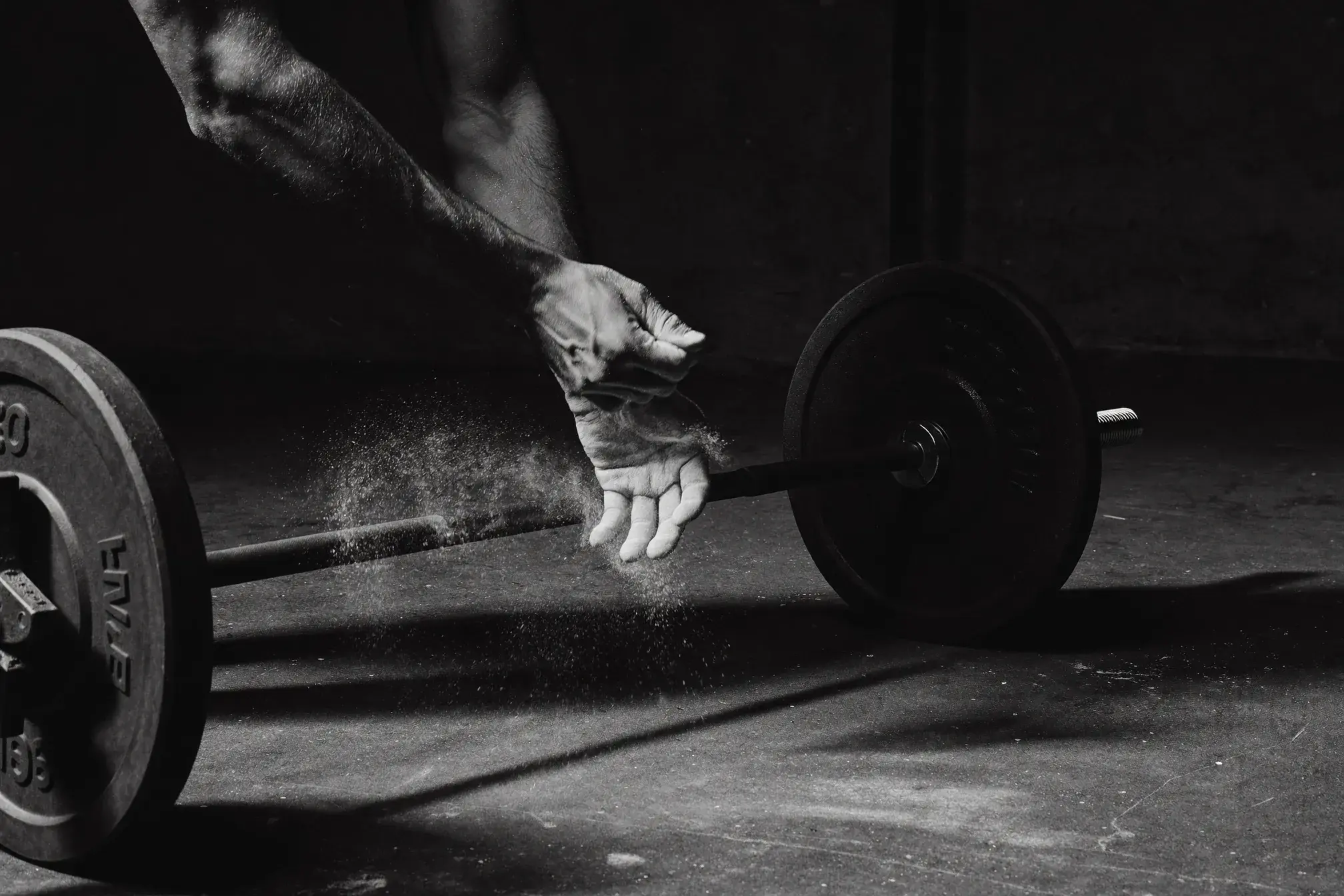 Hands chalking up over a loaded barbell before a squat, dramatic gym lighting — progressive overload for faith-driven athletes