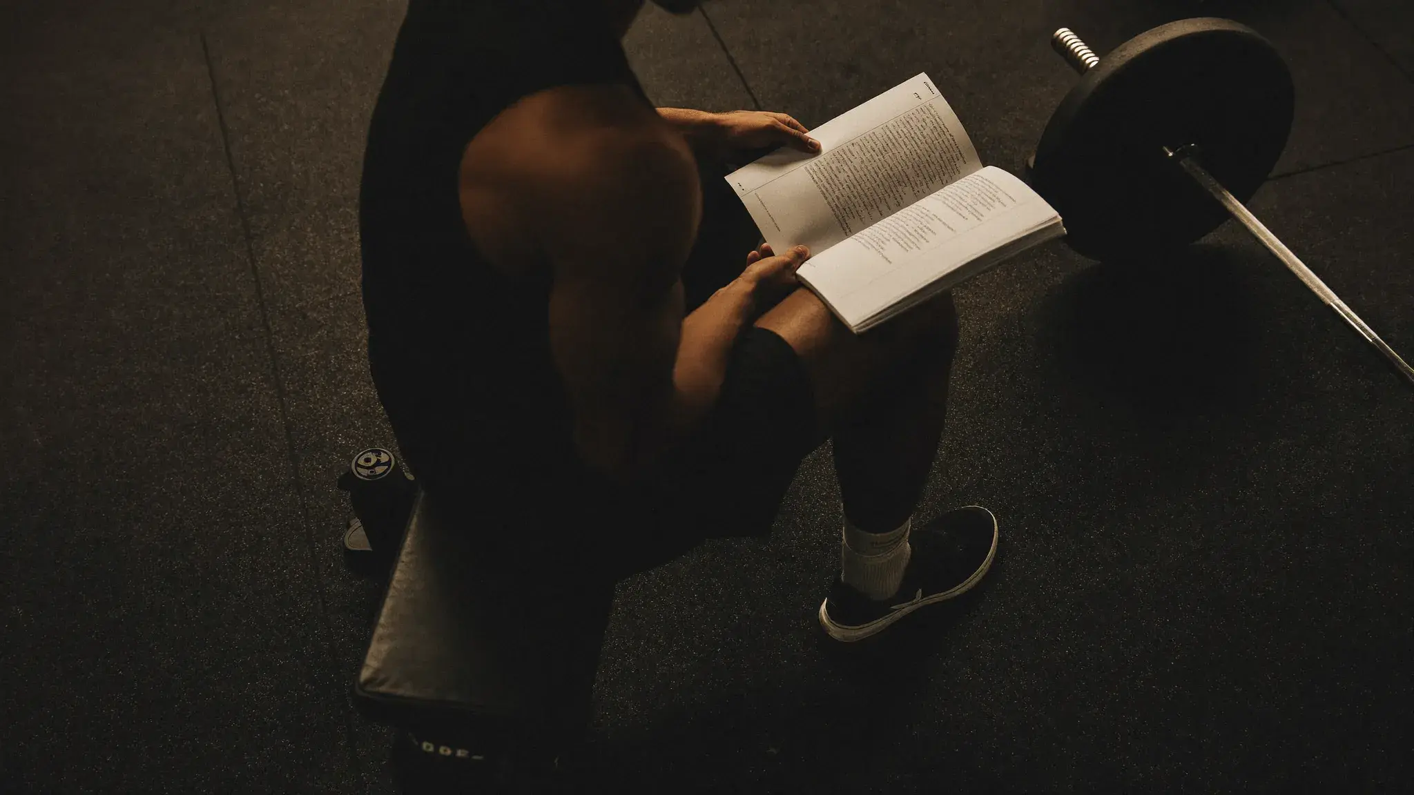 Athlete in a quiet gym, open training log beside a loaded barbell rack - discipline framework for progressive overload